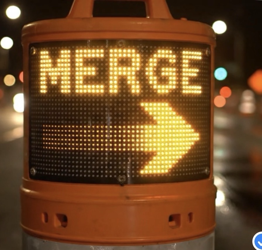 Close-up of a SWZL LED display at night showing the word MERGE with a directional arrow, illuminated amber against a blurred highway background.